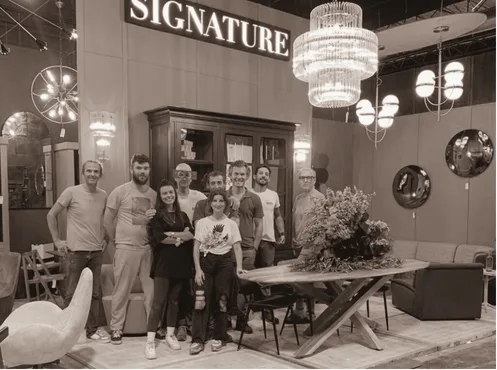L'équipe Signature réunie sur son stand de salon, devant un buffet en chêne massif et sous ses lustres
